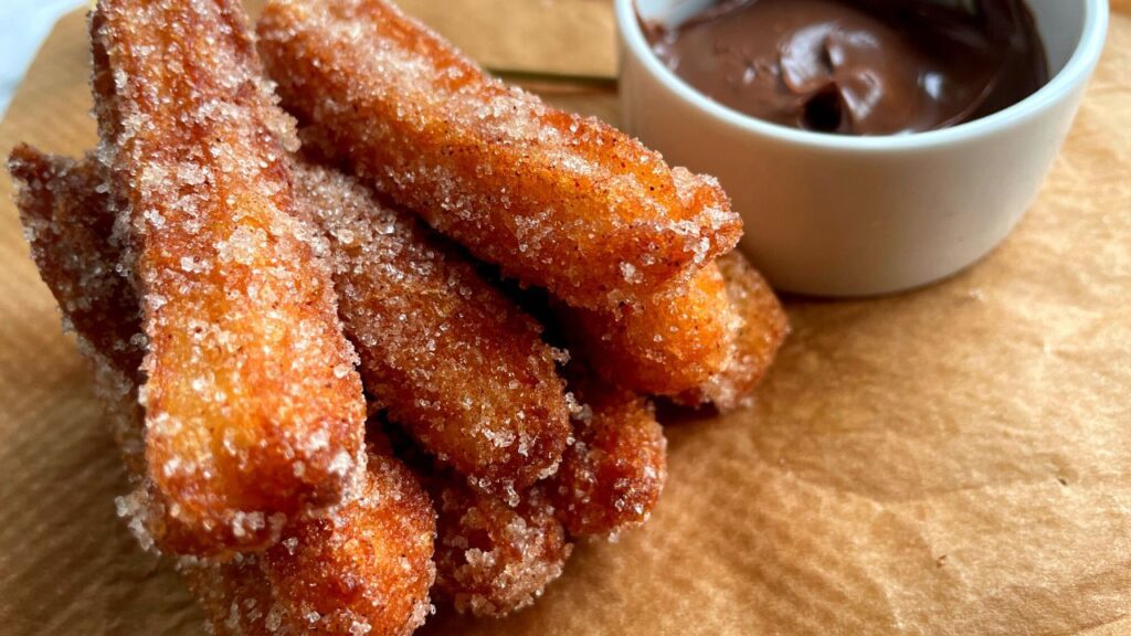 Freshly made Churros in a brown paper with chocolate sauce on side on a small white bowl