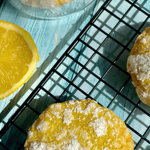 Freshly baked Lemon Crinkle Cookies laid in a cooling rack and a slice of lemon on display