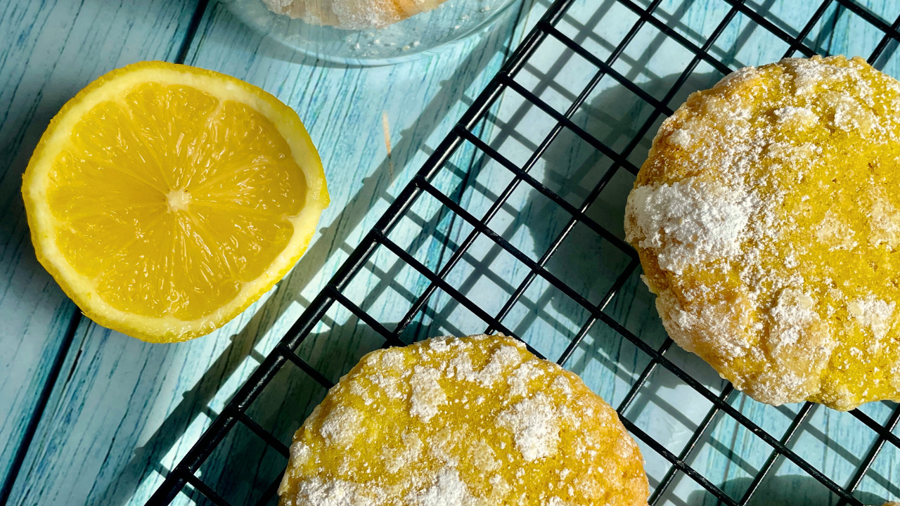 Freshly baked Lemon Crinkle Cookies laid in a cooling rack and a slice of lemon on display