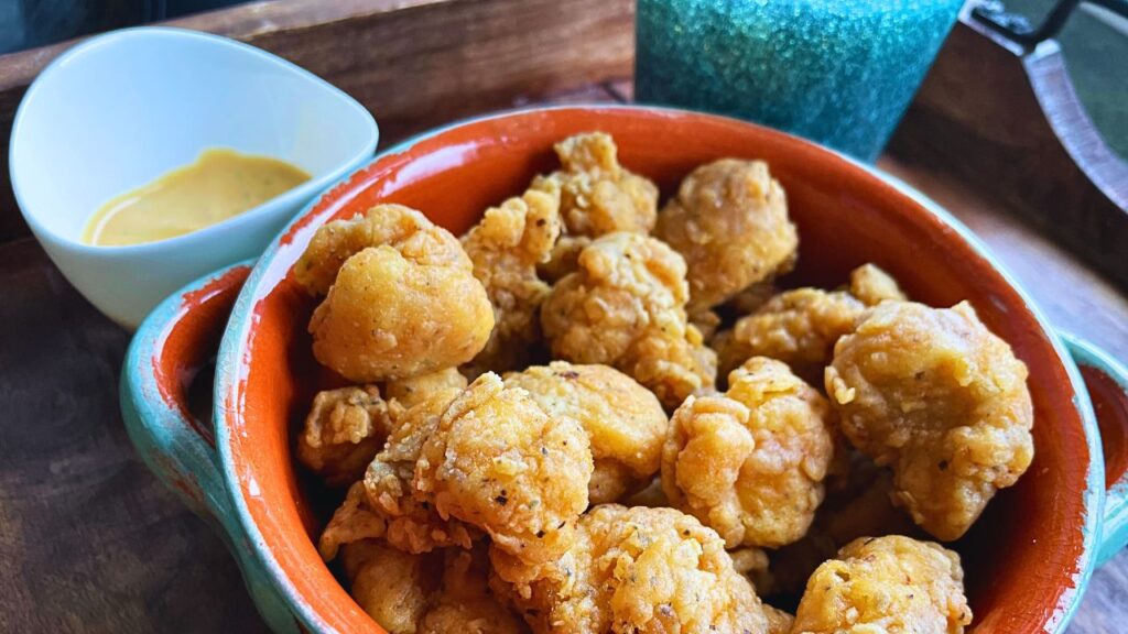 KFC Style Popcorn Chicken served in a earthenware bowl. Yellow sauce served on the side on a white small bowl.