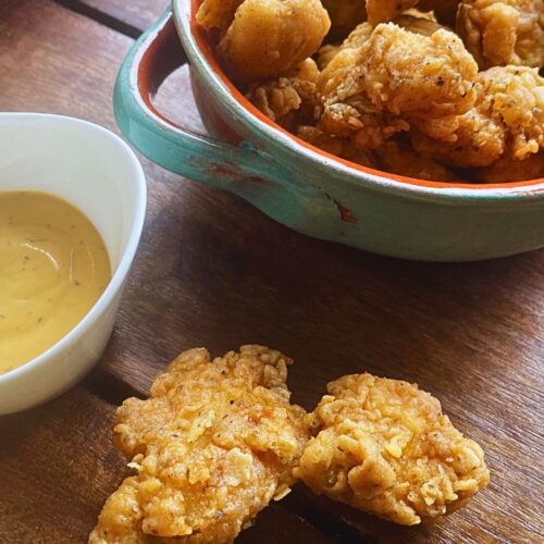 Popcorn chicken served in a blue bowl with dipping sauce on the side on a wooden board