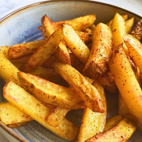 A bowl of freshly air fried, golden-brown potato chips seasoned with spices on a marble countertop.