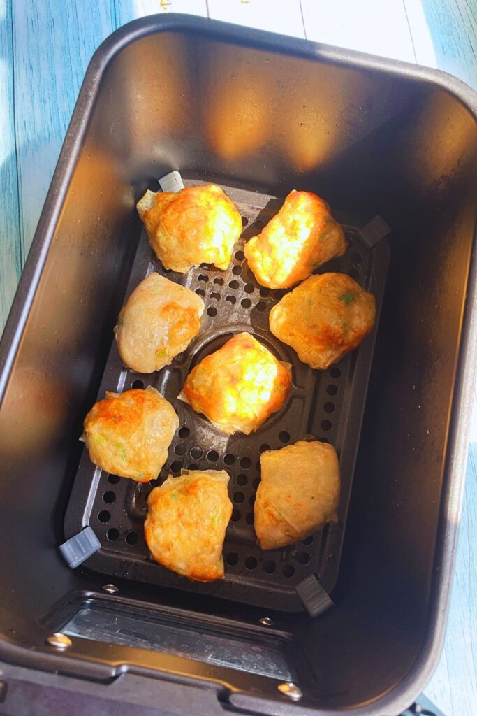 Golden-brown crispy dumplings in black air fryer basket, sitting on a light blue wooden table under natural light.
