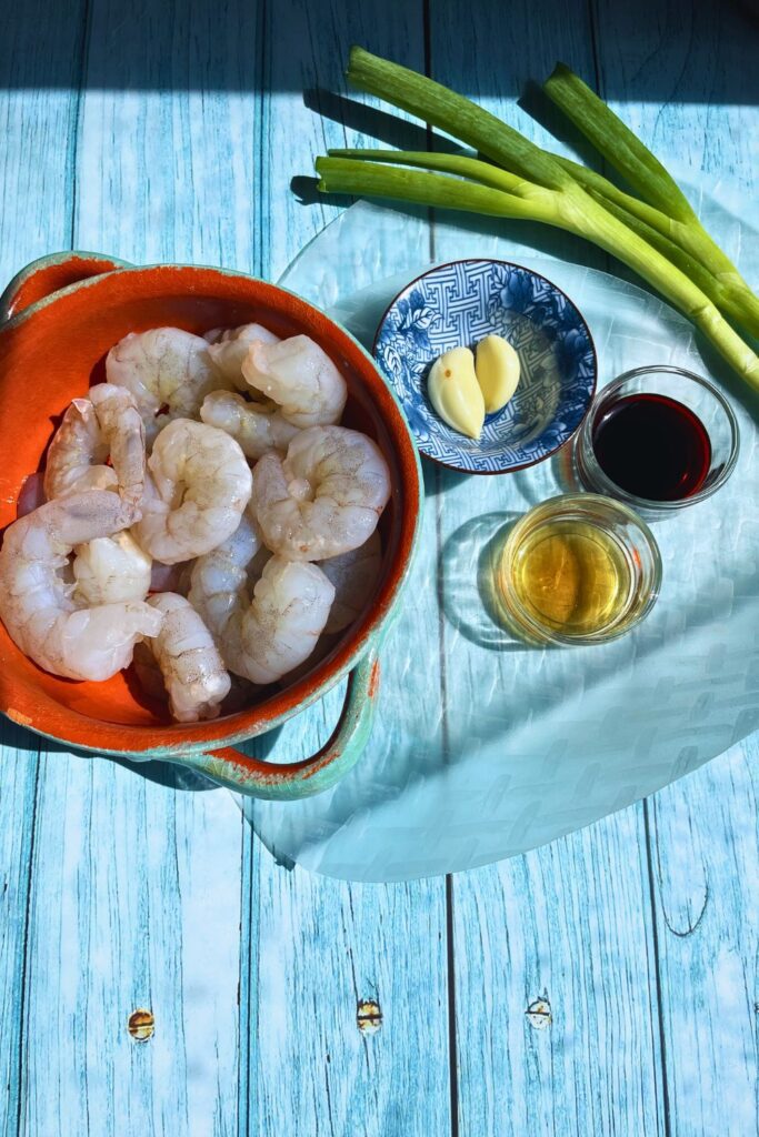 Dumplings ingredients prawns, spring onion, garlic, soy sauce, sesame oil laid in a blue wooden board in partial sunlight.