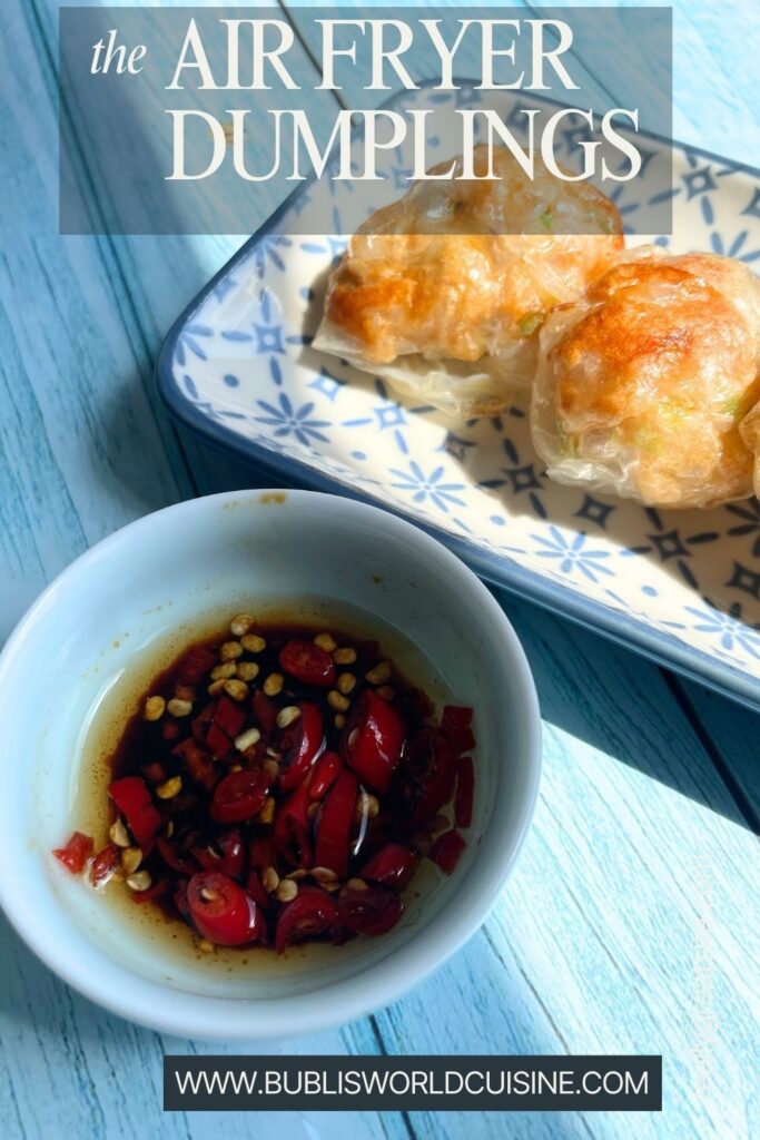 Two golden-brown fried dumplings on a decorative plate next to a bowl of spicy red chili dipping sauce, all placed on a blue wooden table.