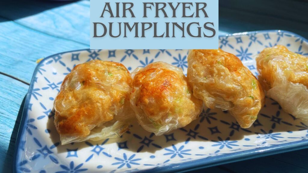 Two golden-brown air fried dumplings on a decorative plate next to a bowl of spicy red chili dipping sauce, all placed on a blue wooden table.