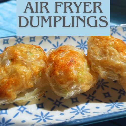 Two golden-brown air fried dumplings on a decorative plate next to a bowl of spicy red chili dipping sauce, all placed on a blue wooden table.