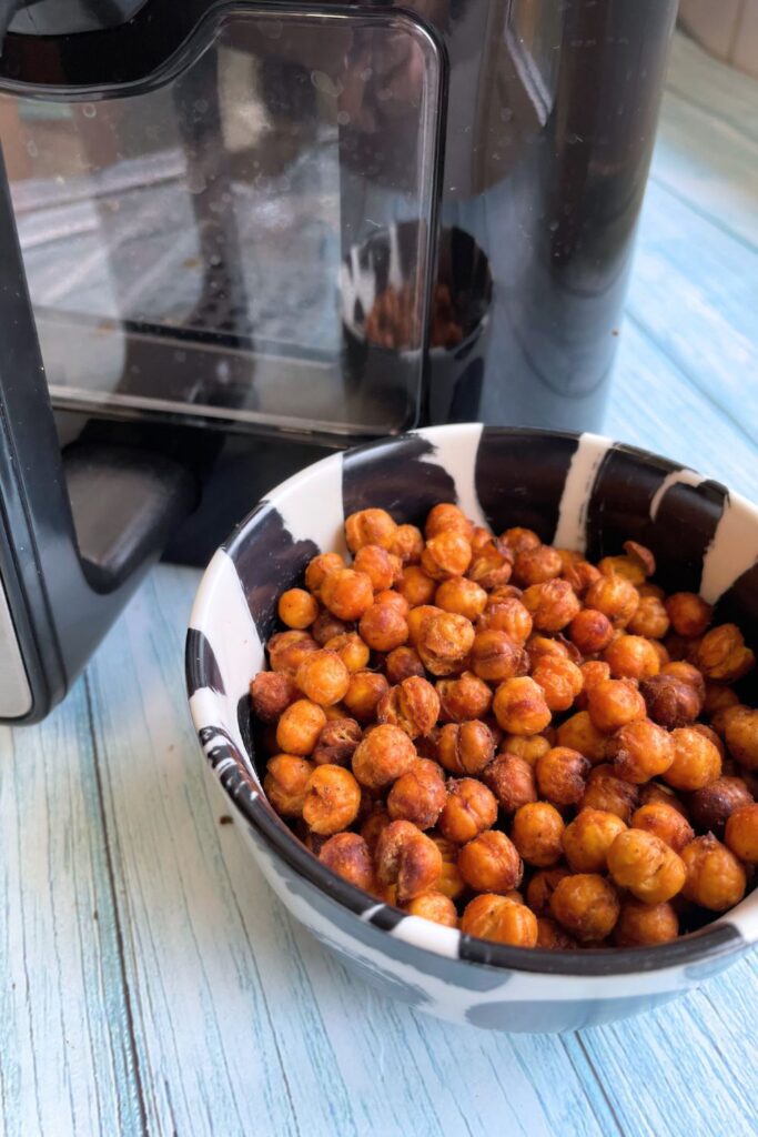 A bowl of crispy air fryer roasted chickpeas next to an air fryer on a light blue wooden surface.