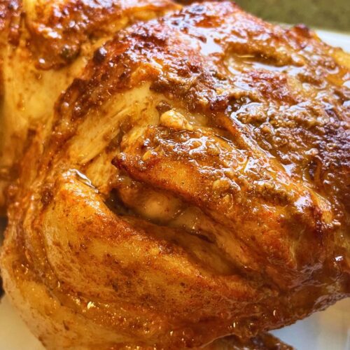 A close-up image of a golden-brown air fryer roasted chicken with crispy skin, served on a white plate. the chicken appears juicy and well-seasoned.