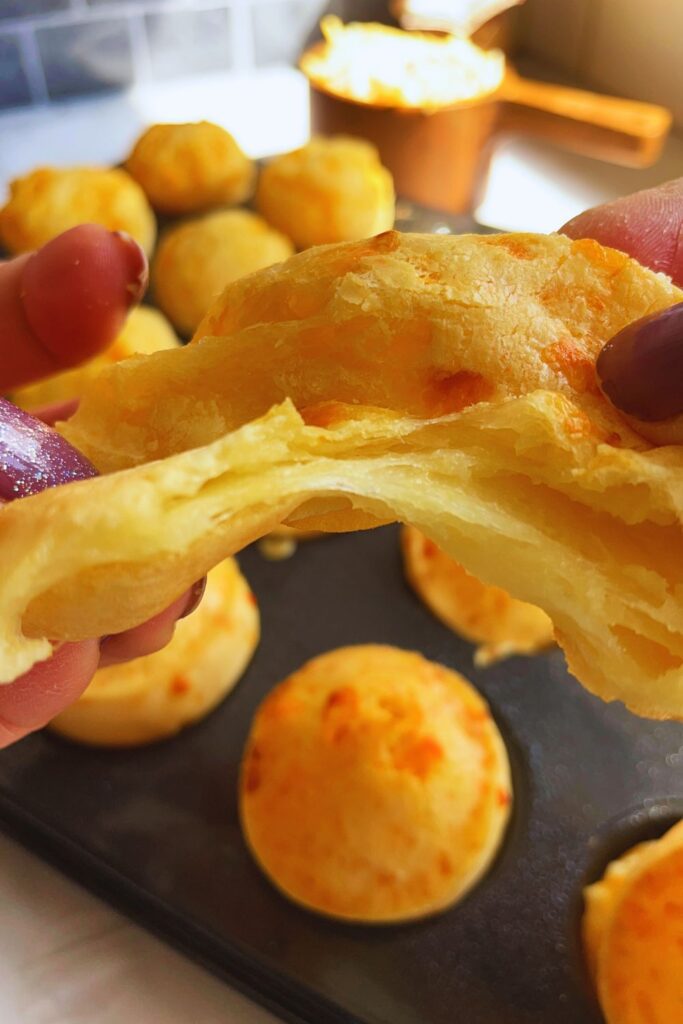 a person holding a piece of Brazilian cheese bread and tearing to show the cheesyness