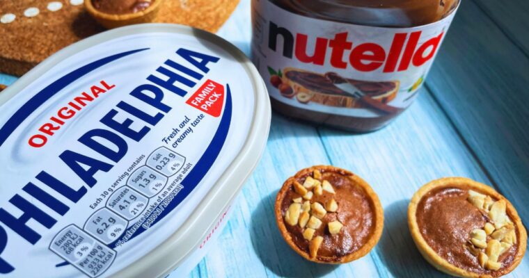 Mini air fryer Nutella tarts on a blue wooden table with Nutella jar on the back and a tub of Philadelphia cream cheese.