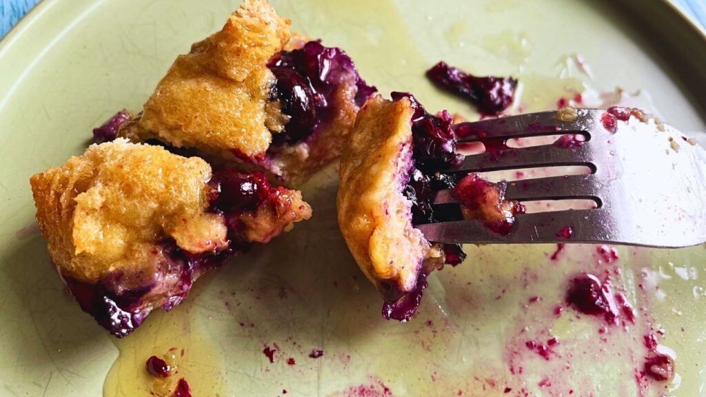 One bite sized Blueberry French Toast Cup served on a plate with some maple syrup and fork