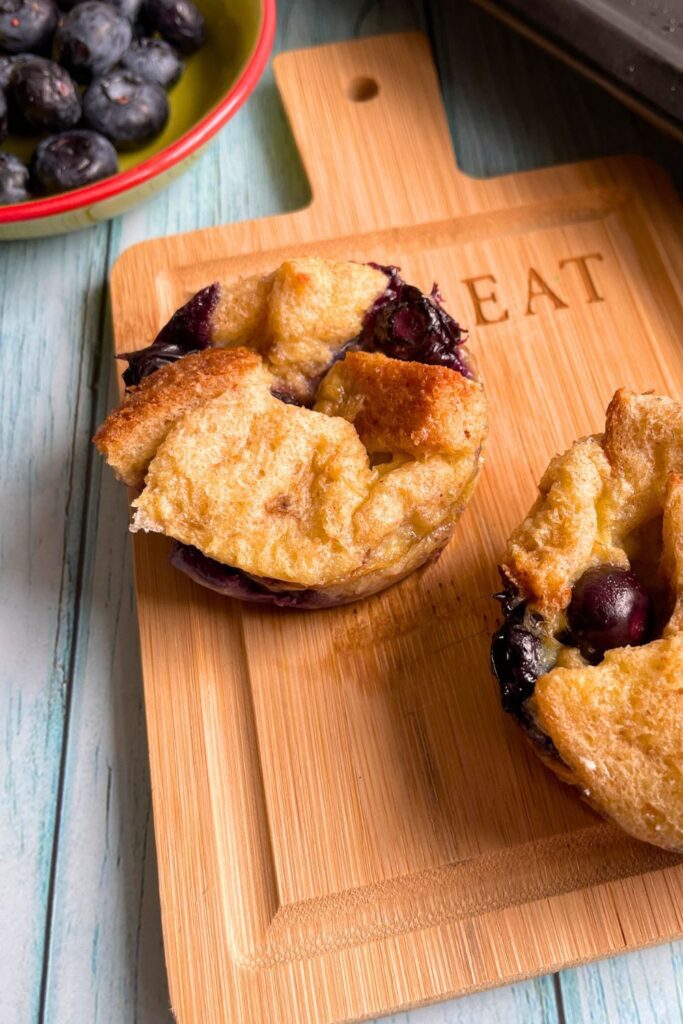 2 Blueberry French Toast Cups served on a wooden board and some fresh blueberries at the back