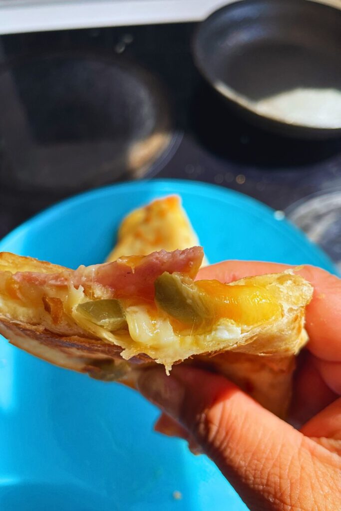 Close up shot of a breakfast quesadilla with gooey cheese and meat inside.