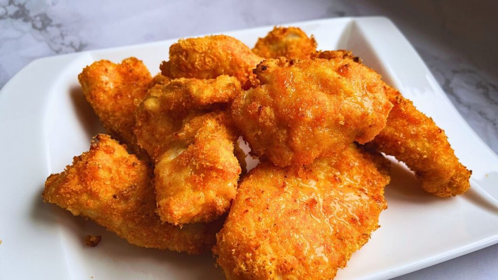 Golden brown freshly air fried crispy chicken tenders are served in a white plate