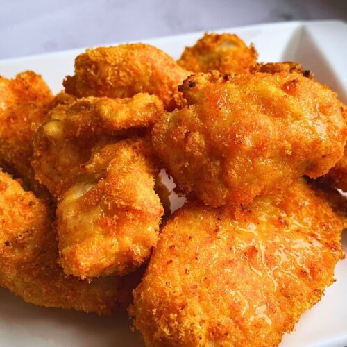 Golden brown freshly air fried crispy chicken tenders are served in a white plate