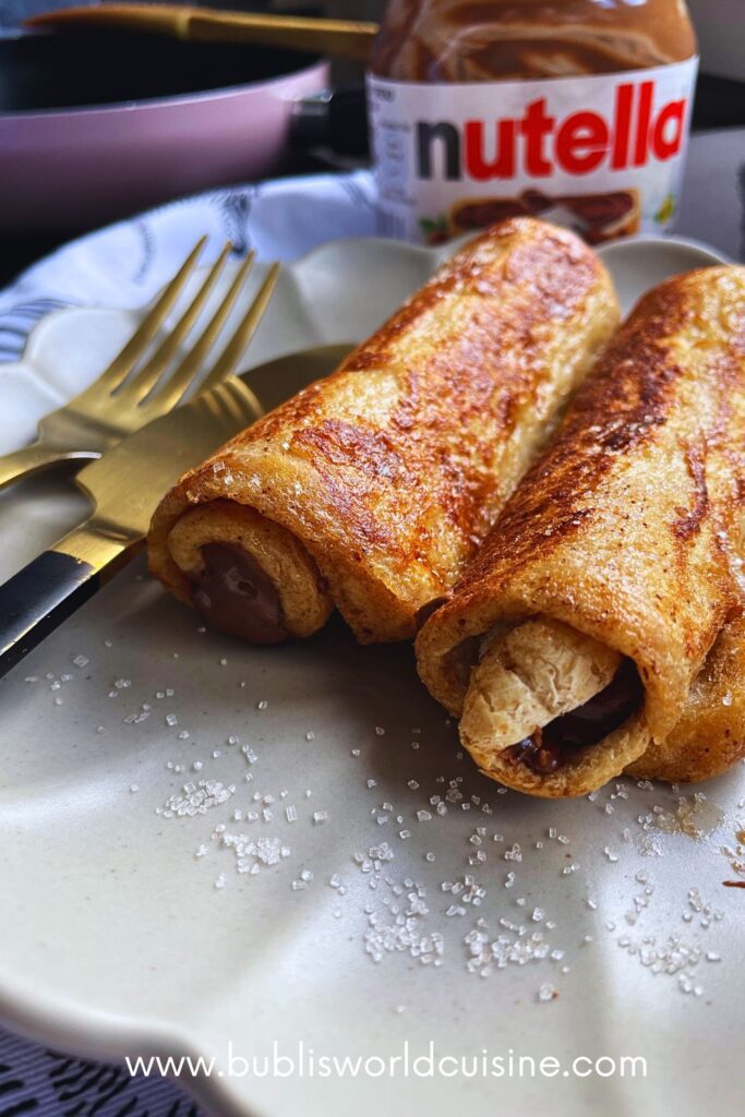 2 Nutella French Toast Rolls served in a grey plate with golden fork and a nutella jar at the back