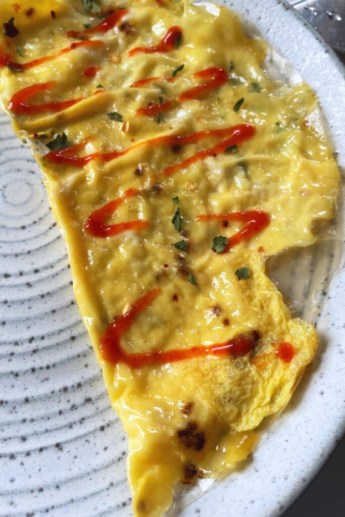 A white plate with  crispy rice paper omelette. A gold knife and fork with black handles are placed to the left of the omelette on the plate. 