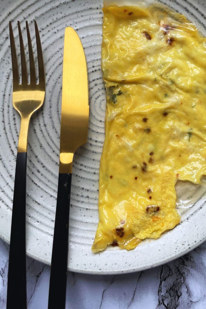 A white plate with rice  paper omelette. A gold knife and fork with black handles are placed to the left of the omelette on the plate. 