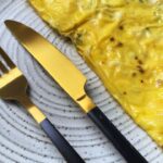 Crispy rice paper omlette served in a beautiful grey plate with golden knife and fork on the left