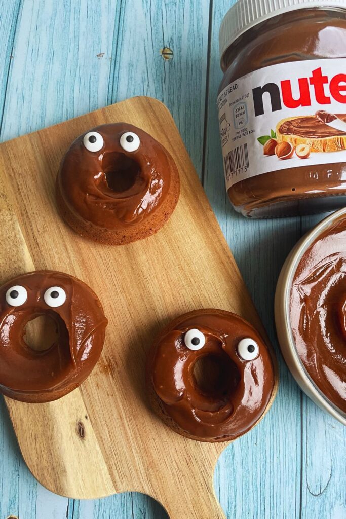 Halloween Special Nutella Monster Donuts served on a wooden board with a nutella jar on the side